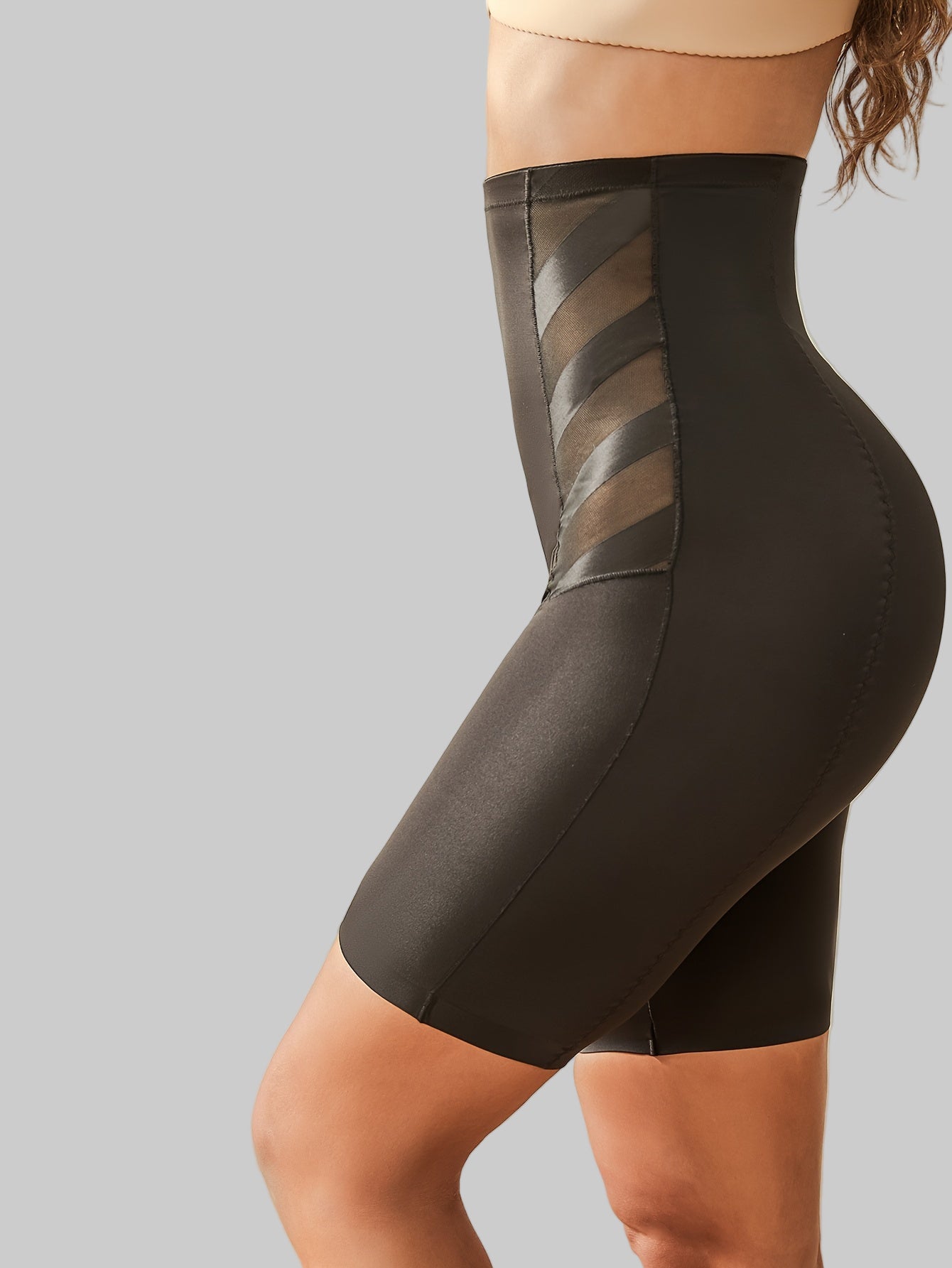 Black shapewear shorts with mesh panels on a gray background